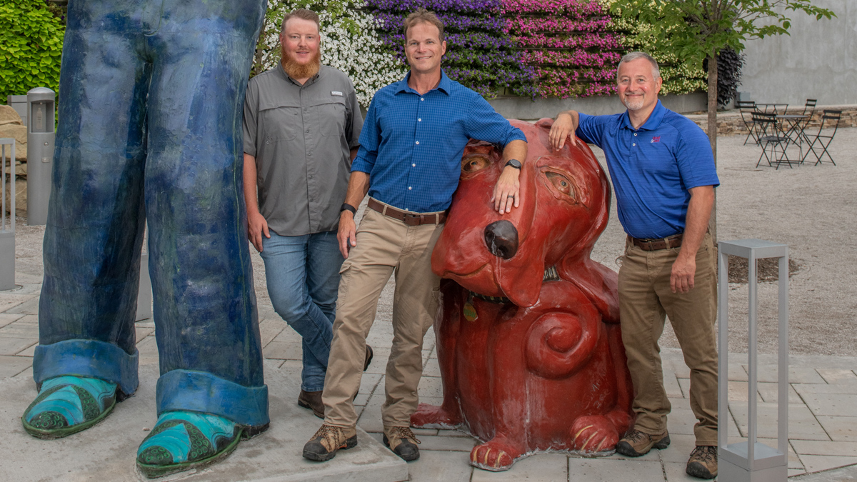 the three team members pose with sculpture from Slack Plaza