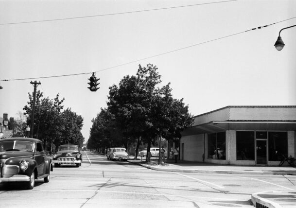 a black and white photo of a car driving down a suburban street
