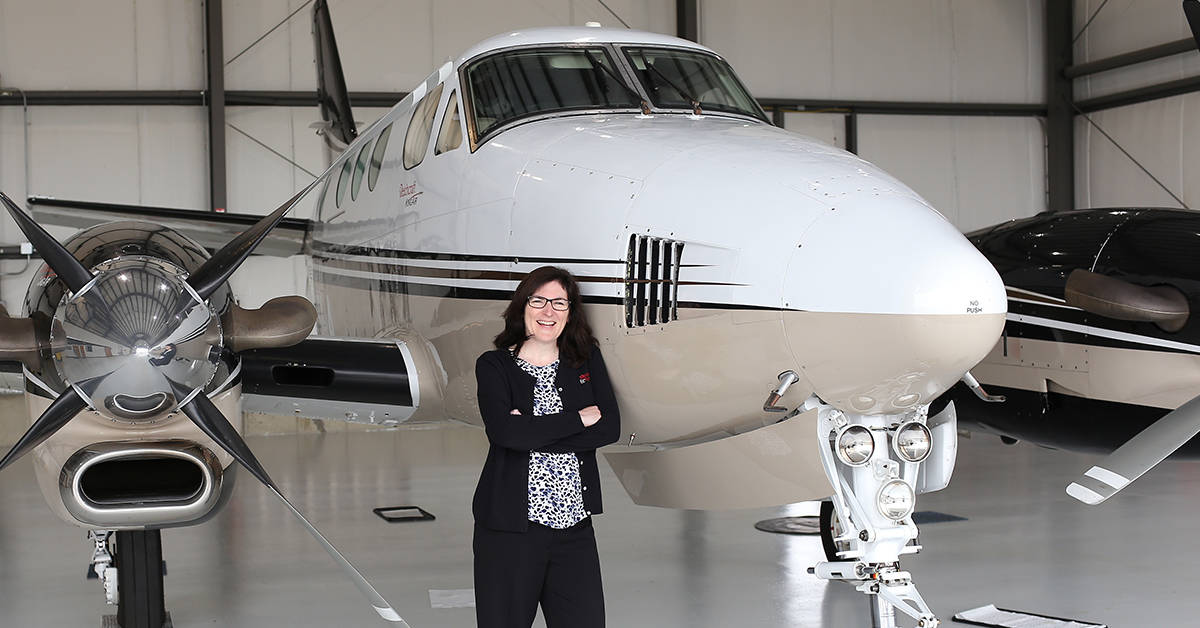 Woman stands in front of an airplane parked in hanger