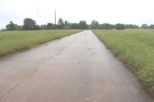 a road under cloudy skies near open fields with trees in the distance