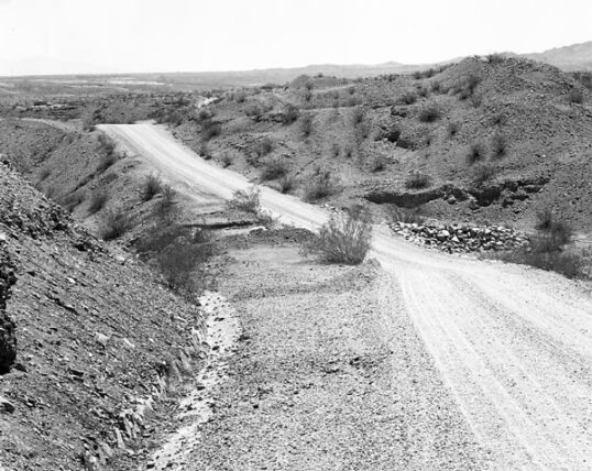 a black and white photo shows a dirt road through the desert