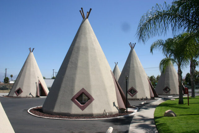 three iconic tipi-shaped structures stand in a paved lot near green palm trees