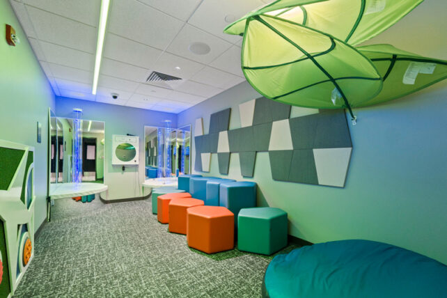 A sensory room at Fort Wayne International Airport featuring soft seating, interactive light features, sensory wall panels, and a suspended cocoon-style swing.