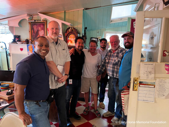 a group of seven people stand in a cozy house with arms around each other