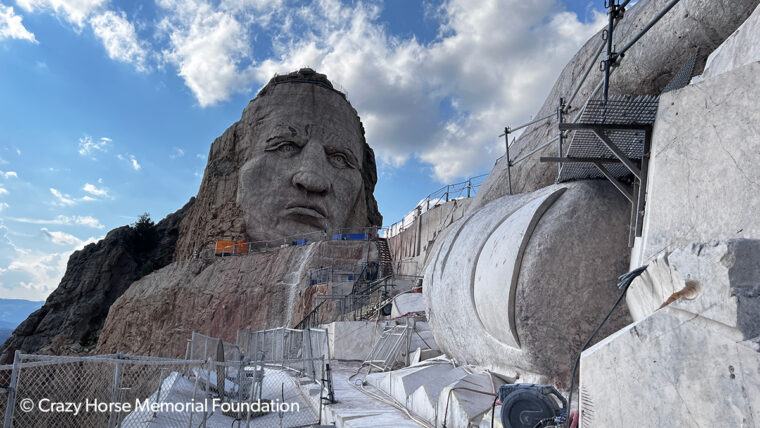 a large native american face is carved into a mountain side his finger protrudes all the way to the camera where it is under construction.