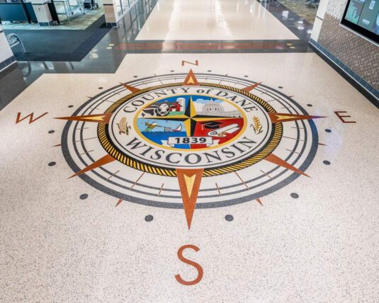 inlaid tiles shows a large compass rose with colorful Dane County seal