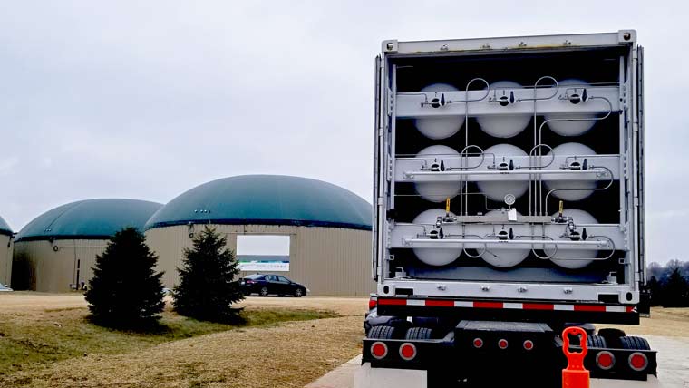 an open truck shows canisters with two domed digester facilities in the background.