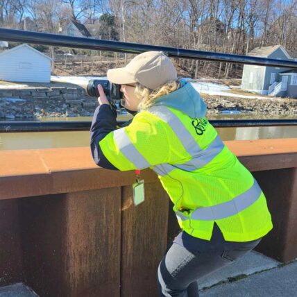 Erin crouches through two rails on a bridge to name a photo with a DSLR camera