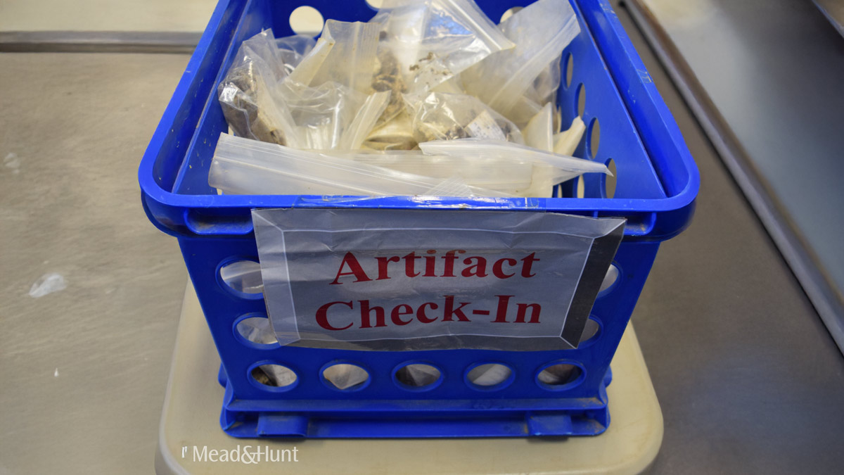 Box of artifacts with a sign on it that says "Artifact Check-In"