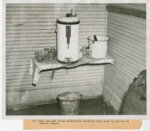 Black and white photo showing a collection of tins and water holders as well as individual jelly juice jars.