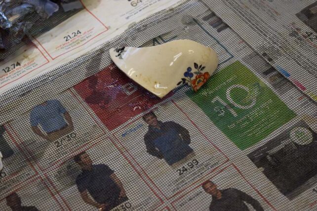 a small, clean fragment of a teacup lays on mesh over some newspaper