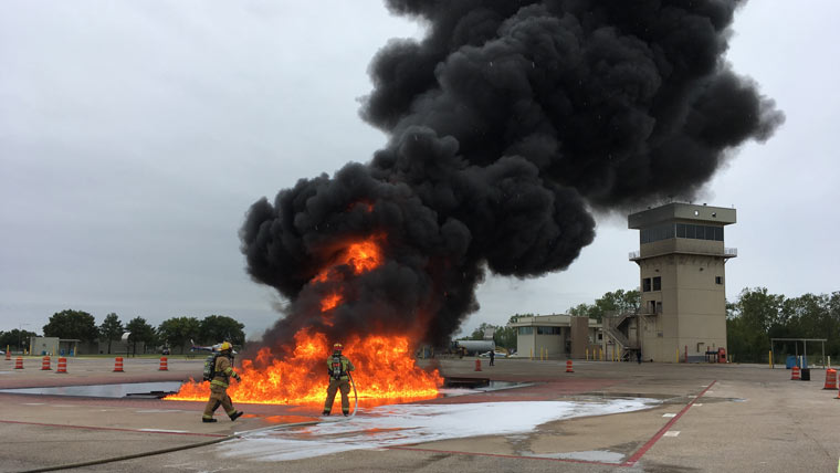 firefighters demonstrate flourine free foam on an airport runway with large flames and black smoke