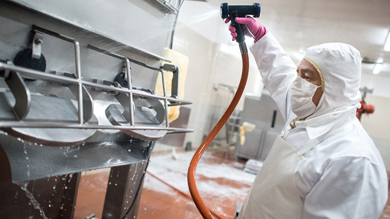 Man in safety attire cleaning food facility equipment