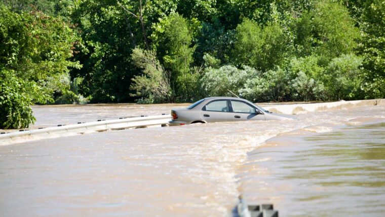 a small sedan floats against a guardrail on a flooded road