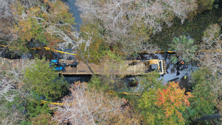 aerial shot showing top-down construction of a boardwalk over water surrounded by trees