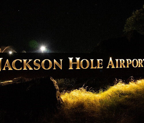The main sign for Jackson Hole Airport is lit up in a soft yellow light under a dark sky