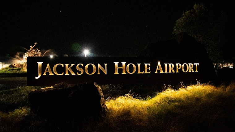 The main sign for Jackson Hole Airport is lit up in a soft yellow light under a dark sky