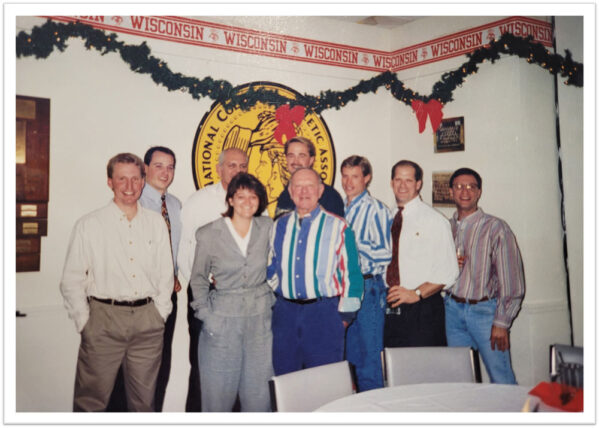 nine people pose in 90s clothes under a christmas garland