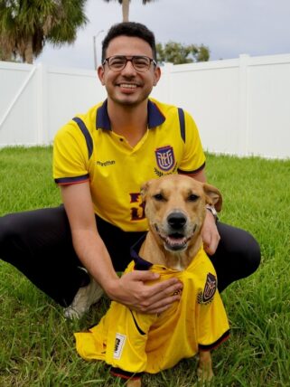 Marcos poses with his dog in his backyard, sporting matching Ecuador jerseys, to support the team during the World Cup tour.