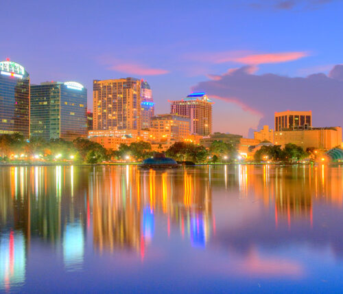 Orlando cityscape at dusk with buildings lit up and reflecting off lake