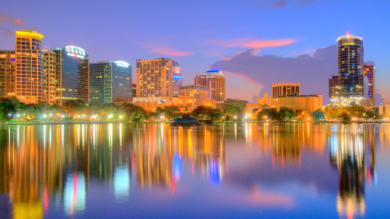 Orlando cityscape at dusk with buildings lit up and reflecting off lake