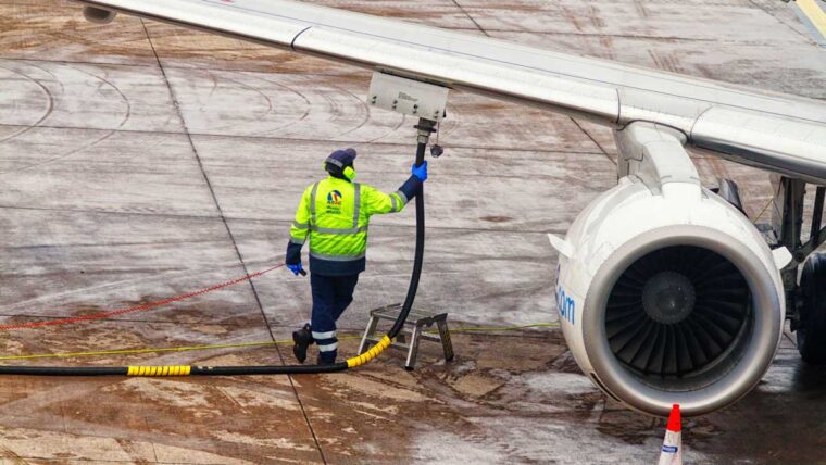 a worker holds a fuel hose that's connected to the wing of an airplane