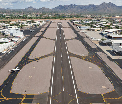 view looking down full runway with taxiways on each side, plane on left taxiway, mountains in the background