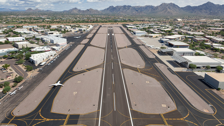 view looking down full runway with taxiways on each side, plane on left taxiway, mountains in the background