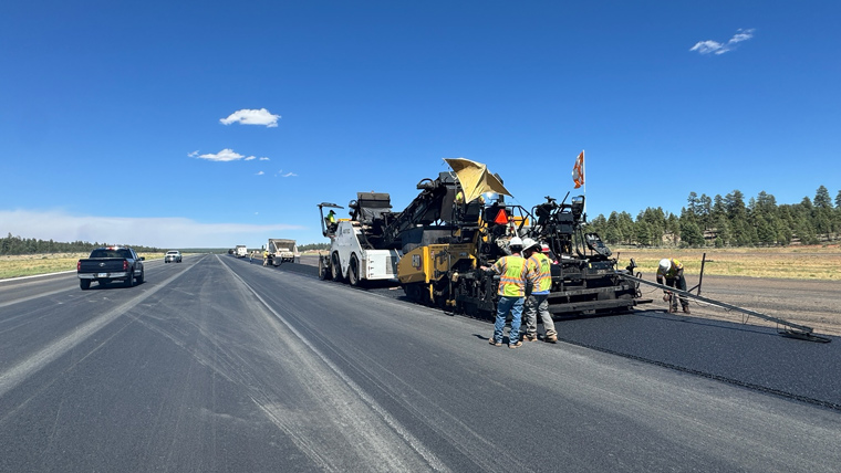 Wide shot of construction crew laying asphalt with clear sky