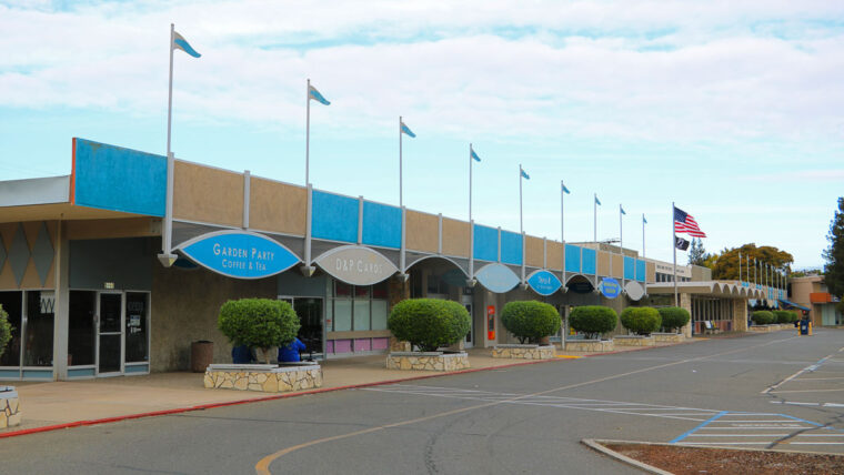 a one-story shopping center has alternating blue and tan sections with flags from the top in an art-deco style