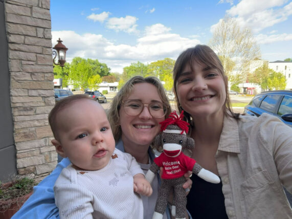 Erin and her wife pose with a baby boy and toy sock monkey from Mead & Hunt
