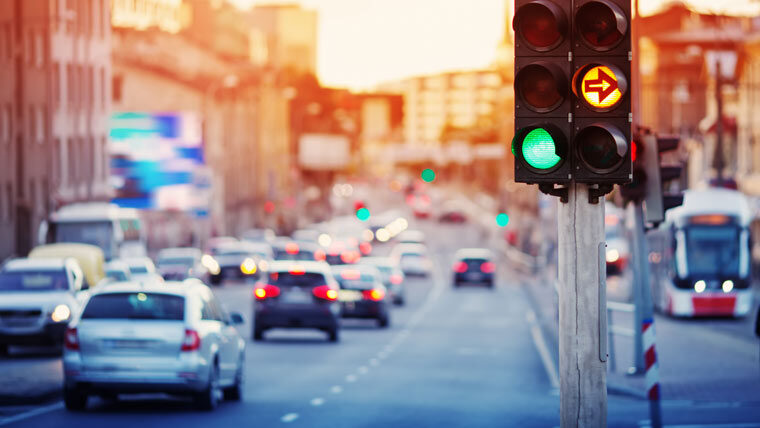 a traffic light is in focus with cars at dusk in background