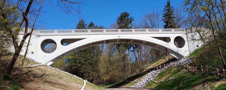 a beautiful concrete bridge spans a ravine among green trees and a blue sky