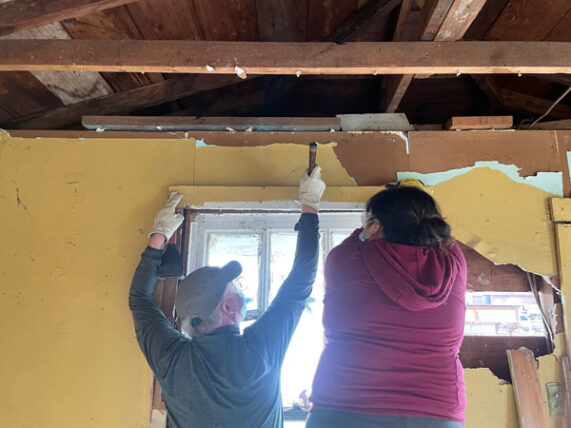 two people remove drywall over a window