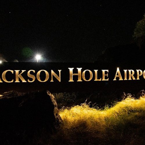 The main sign for Jackson Hole Airport is lit up in a soft yellow light under a dark sky