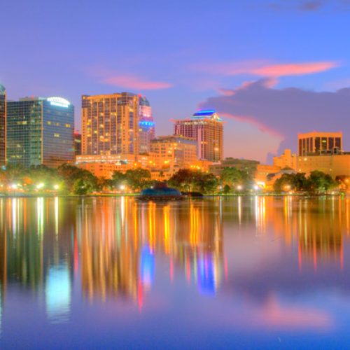 Orlando cityscape at dusk with buildings lit up and reflecting off lake