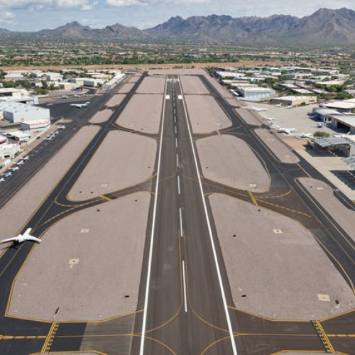 view looking down full runway with taxiways on each side, plane on left taxiway, mountains in the background