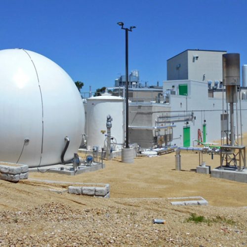 large, round digester near other buildings on a sunny day