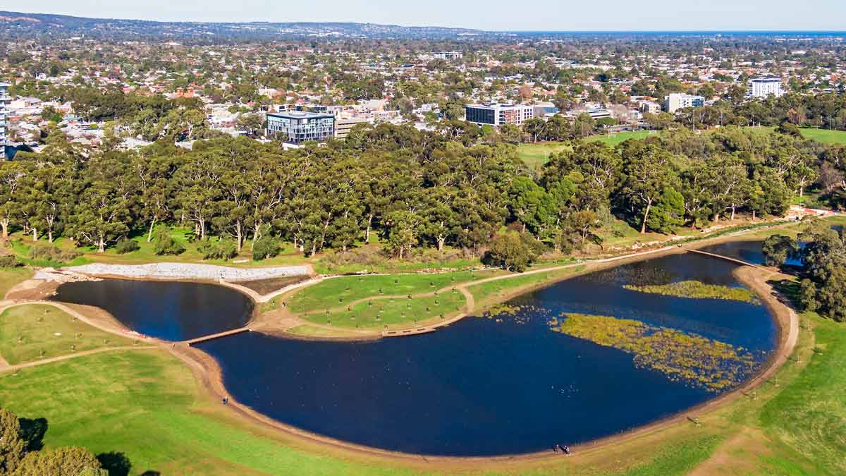 Aerial sunny view new stormwater wetlands in Adelaide public park with residential and office buildings in background