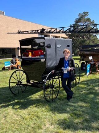 Mary is pictured next to an Amish buggy for which Hentzen Coatings supplied the black paint.