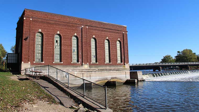 a large brick building next to a small dam on a river on a sunny day