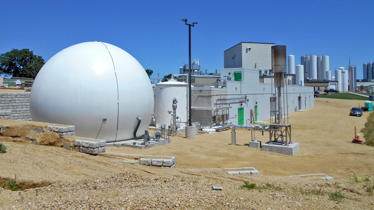 large, round digester near other buildings on a sunny day