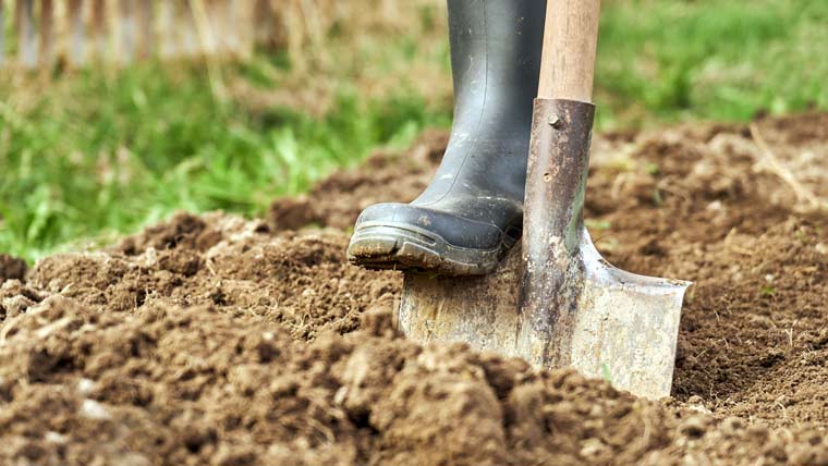 a boot pushes a shovel into a pile of dirt