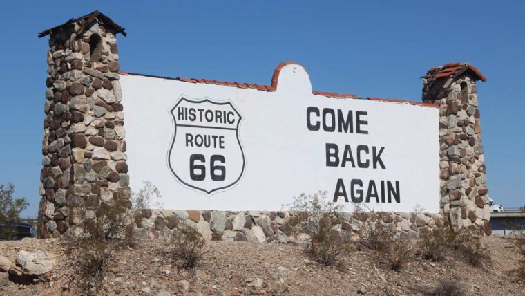 a large sign has the Route 66 sign with come back again in big black letters