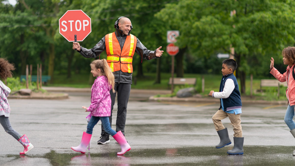 a crossing guard helps children cross the street in bright rain gear