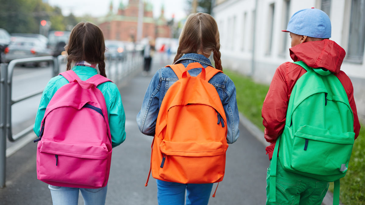 Backs of schoolkids with colorful rucksacks moving in the street