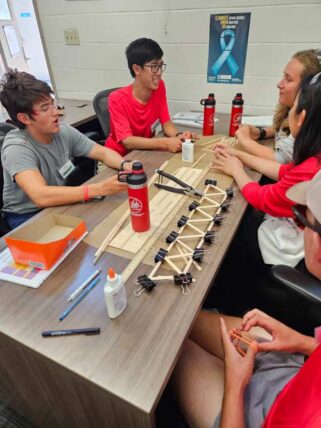 students sit around a table working with popsicle sticks on a project.