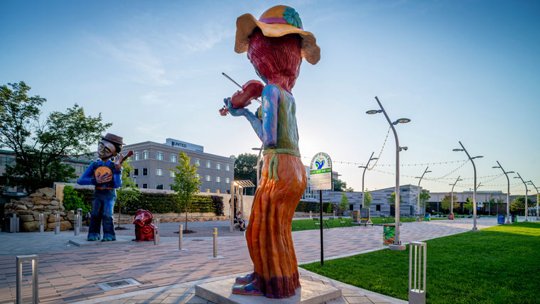 a larger than life sculpture depicts an Appalachian woman playing a fiddle in Slack Plaza