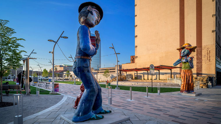a larger than life sculpture depicts an Appalachian man playing a banjo in Slack Plaza