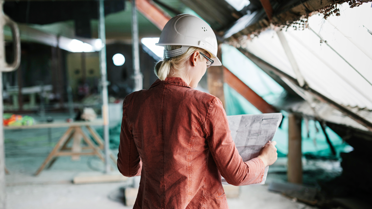 a woman wears a hardhat and looks at a blueprint in a construction site